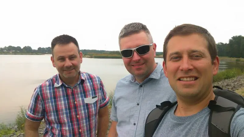 trzech mężczyzn robiących sobie selfie przed jeziorem